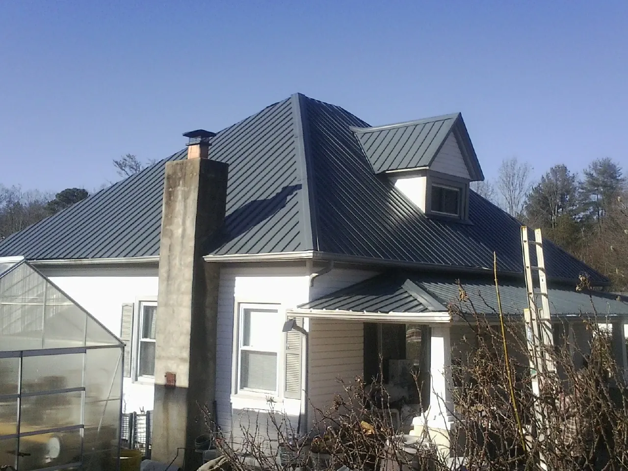 Dark blue standing seam metal roof on a white farmhouse with dormer — Slate & Tile Roof Repair by Roofing Brothers in Lindsey