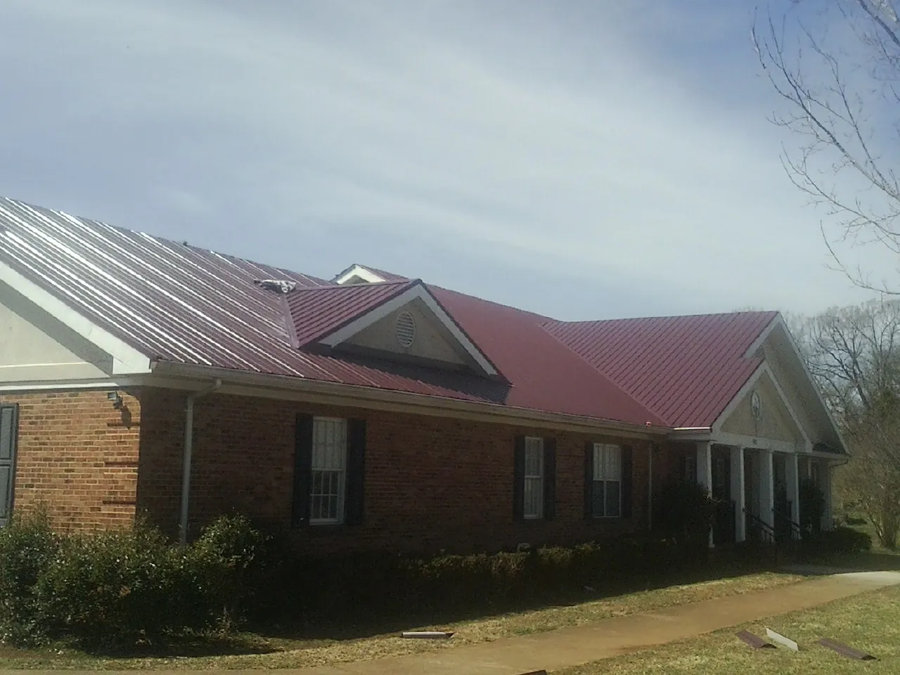 Red metal roof with gabled entries on a long brick building, from a Hail Damage Roof Repair job in Lindsey