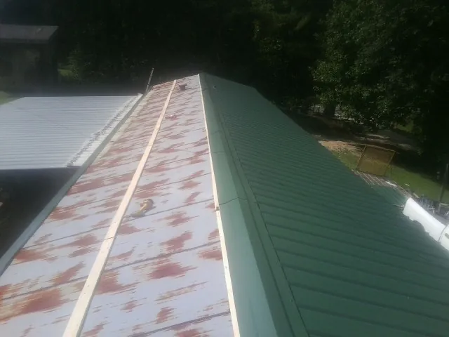 Old rusted panels beside newly installed green metal roofing — Wind Damage Roof Repair by Roofing Brothers in Lindsey