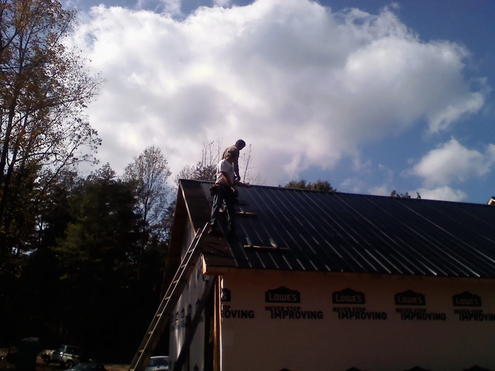 Roofer fastening dark metal panels high against a cloudy sky, from a Roof Inspection job in Lindsey