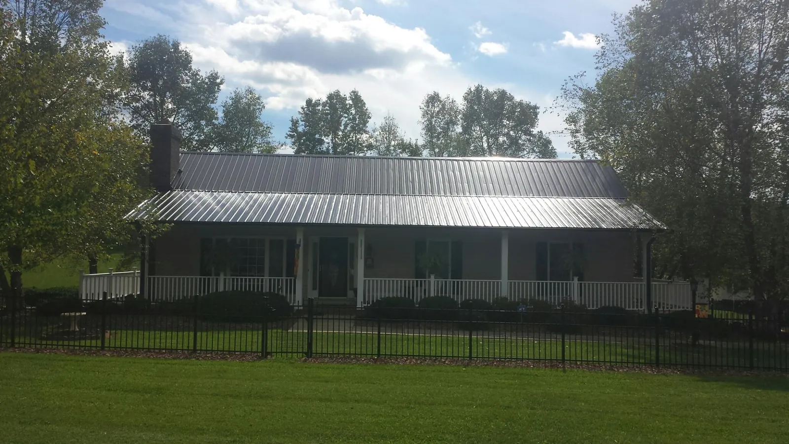 Gray metal roof on a brick ranch with a full width front porch — Gutter Guard Installation work by our crew in Lindsey