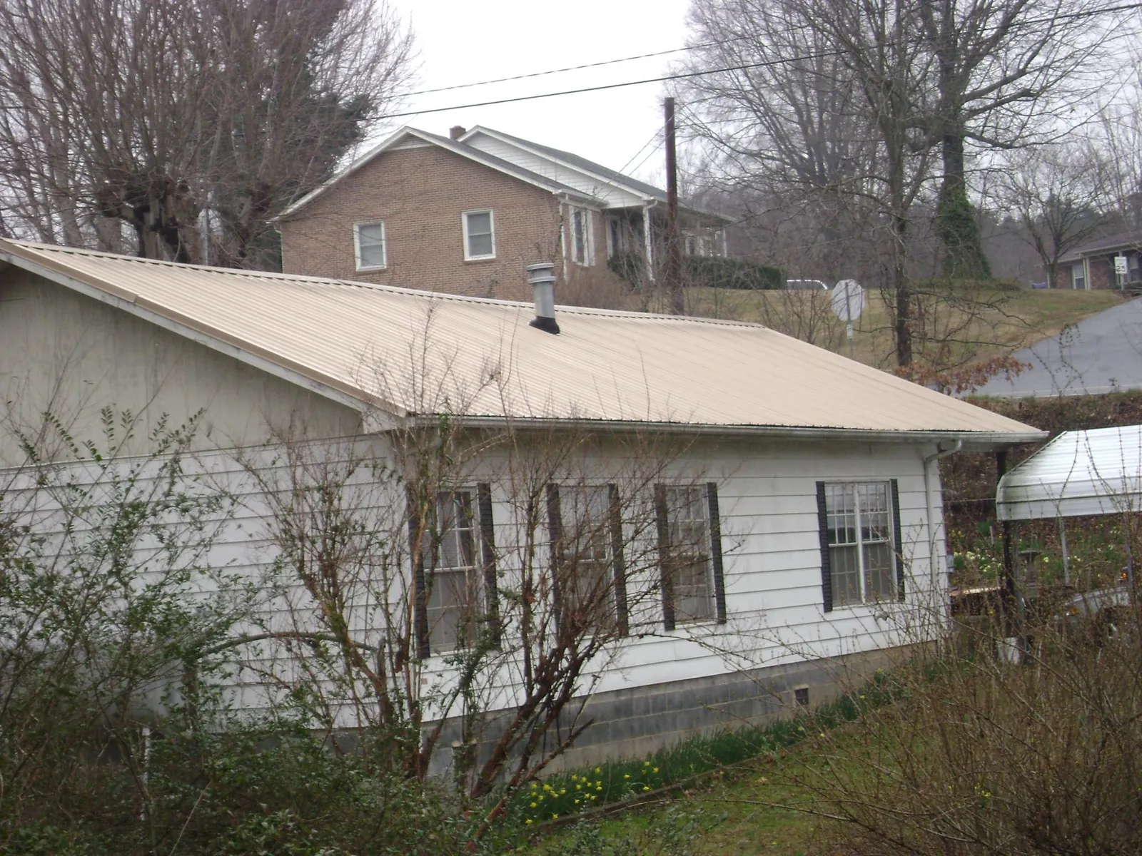 Tan metal roof on a white sided house set into a hillside — Commercial Roofing by Roofing Brothers in Lindsey
